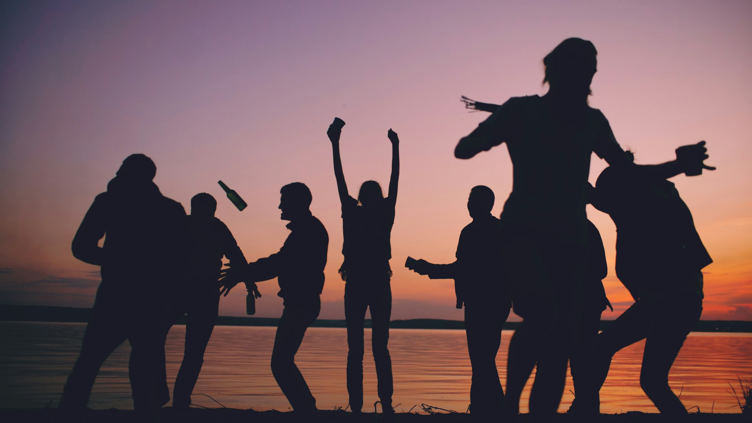 Friends dancing on the beach at sunset, seen in silhouette